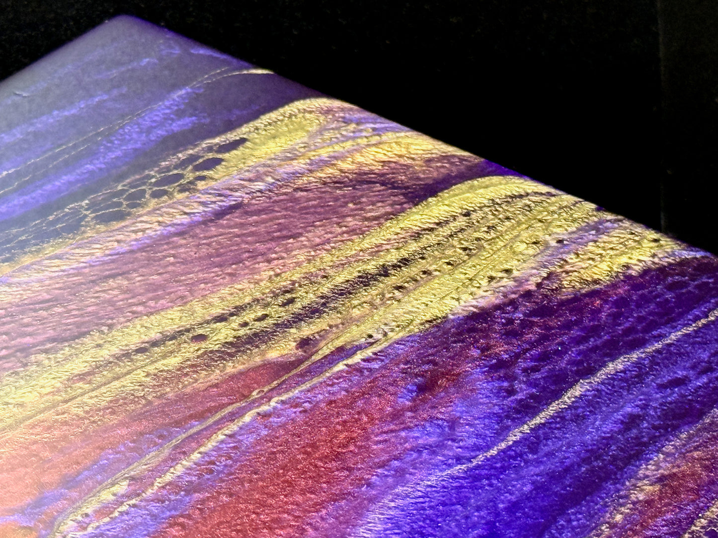 Colorful abstract painting with wavy patterns in purple, gold, and yellow on a dark background.